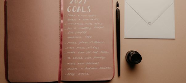 Open notebook with 2021 goals, calligraphy pen, envelope, and ink jar on neutral background.